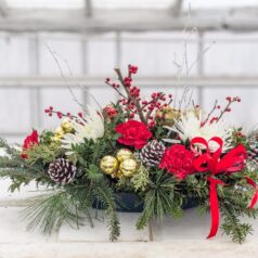 A christmas arrangement of pine cones, red flowers and greenery.