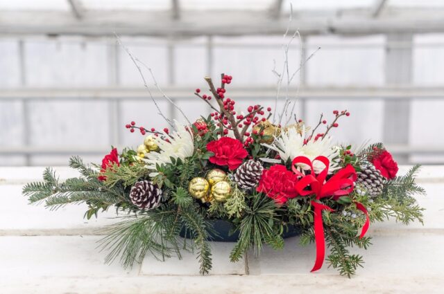 A christmas arrangement of pine cones, red flowers and greenery.