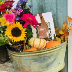 A bucket of flowers and pumpkins on the porch.