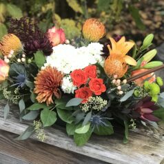 A wooden table with flowers and greenery on it.