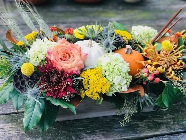 A wooden table with flowers and pumpkins on it.
