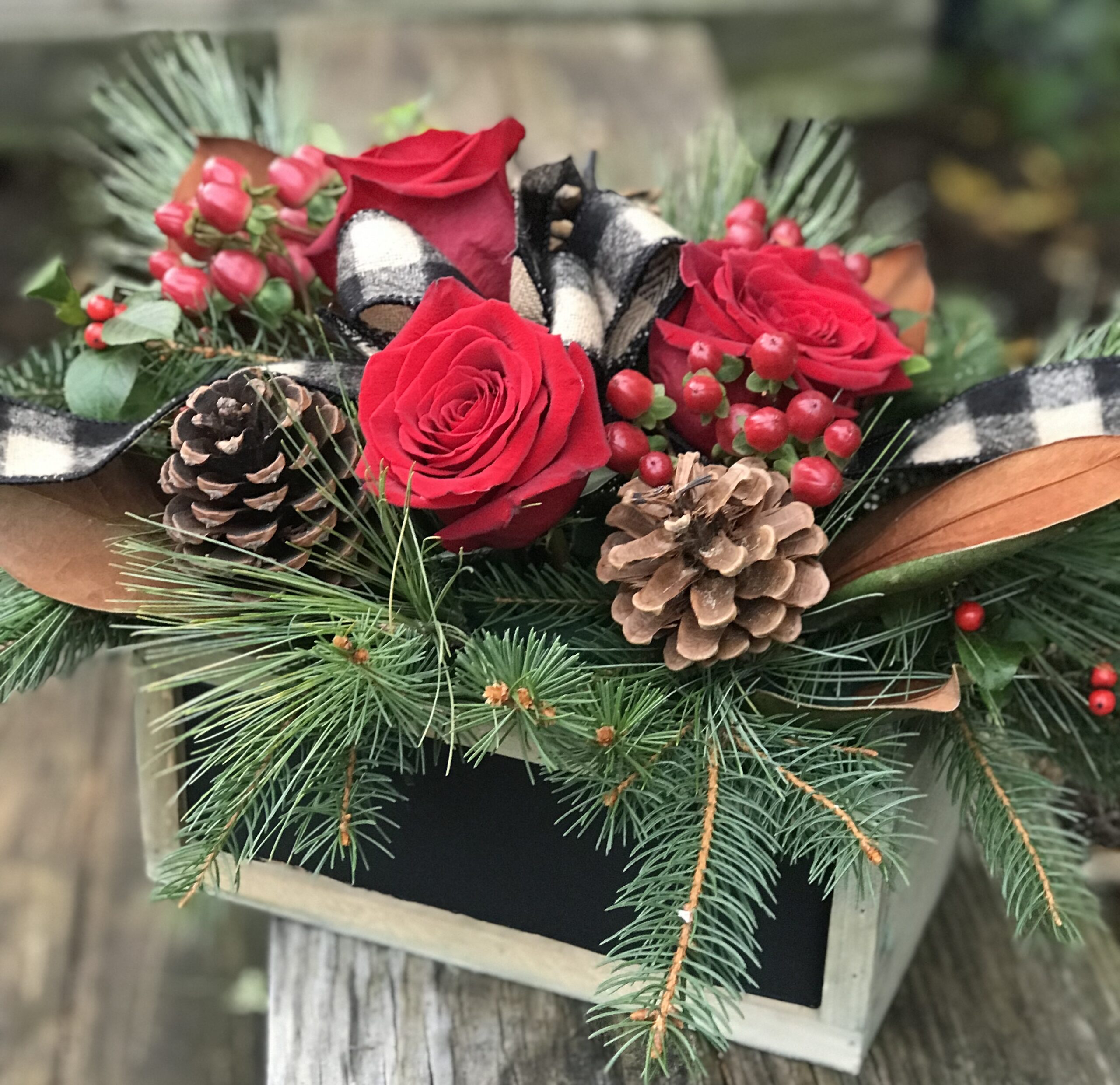 A wooden box with pine cones and roses in it.