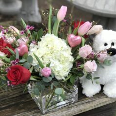 A white teddy bear sitting next to a vase of flowers.