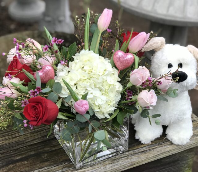 A white teddy bear sitting next to a vase of flowers.