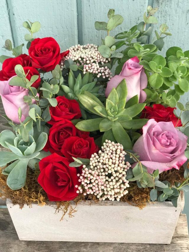 Roses, succulents, and greenery in wooden box.